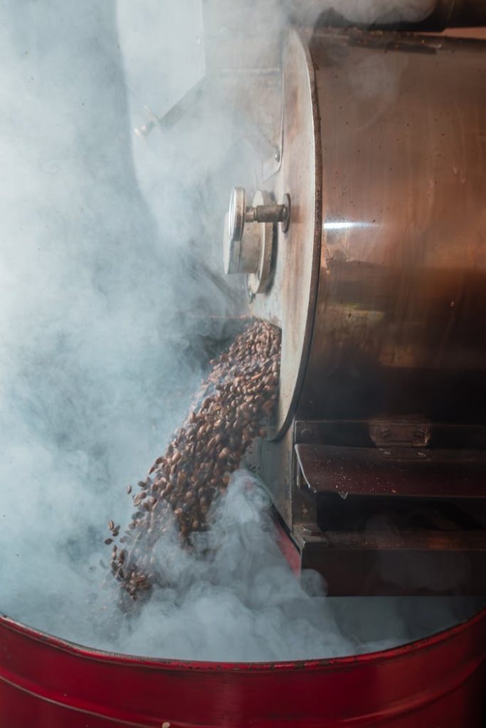 pexels photo 31890551 Steaming coffee beans pouring from an industrial roaster, surrounded by smoke