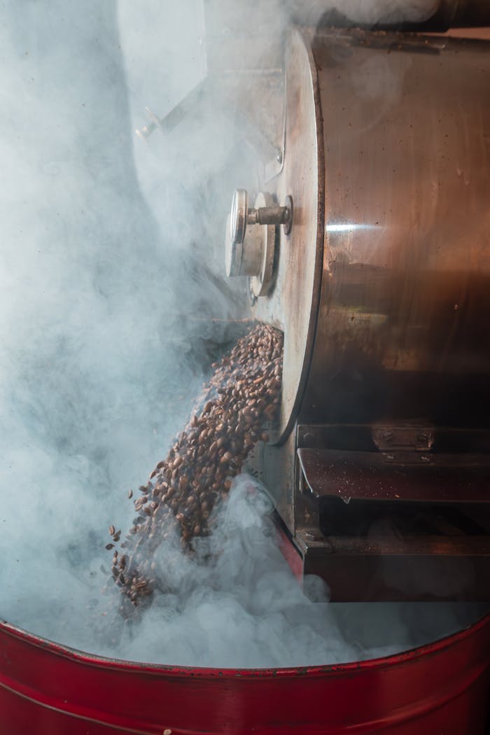 Steaming coffee beans pouring from an industrial roaster, surrounded by smoke