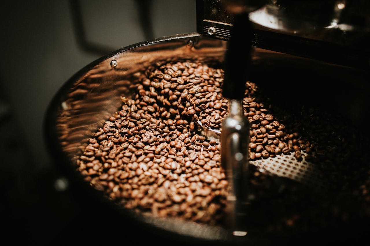 services-02 Close-up of freshly roasted coffee beans in a large industrial coffee roaster, showcasing rich textures and warm tones.
